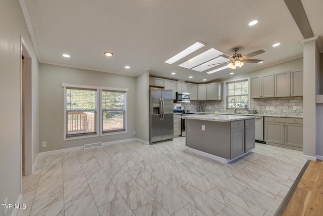 kitchen with a skylight, a center island, decorative backsplash, appliances with stainless steel finishes, and gray cabinetry