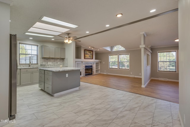 kitchen with light stone countertops, a stone fireplace, a center island, ornamental molding, and ceiling fan