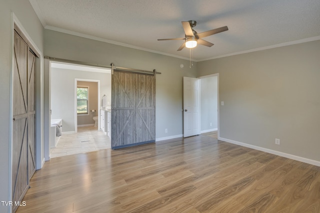 empty room featuring ornamental molding, a textured ceiling, light hardwood / wood-style flooring, ceiling fan, and a barn door