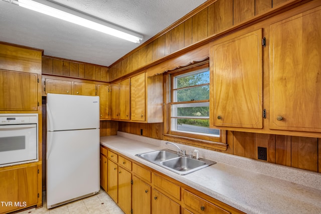 kitchen with a textured ceiling, white appliances, light tile patterned floors, sink, and wooden walls