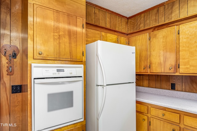 kitchen featuring a textured ceiling, white appliances, and wooden walls