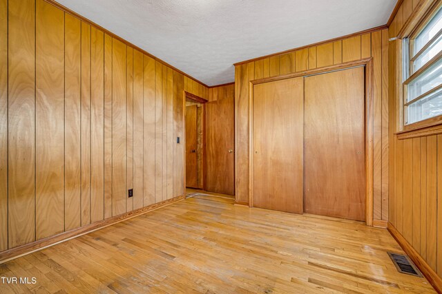 unfurnished bedroom with a closet, light hardwood / wood-style floors, wood walls, and ornamental molding