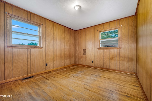 empty room featuring a textured ceiling, wooden walls, and light hardwood / wood-style floors