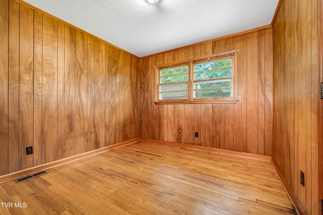 spare room with a textured ceiling, wood walls, and light hardwood / wood-style floors