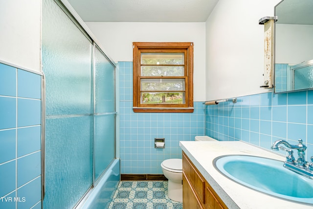 full bathroom featuring toilet, tile walls, bath / shower combo with glass door, decorative backsplash, and vanity