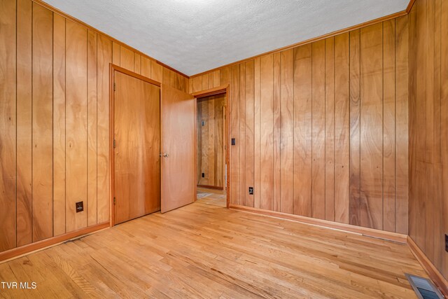 spare room featuring wooden walls, a textured ceiling, and light hardwood / wood-style flooring