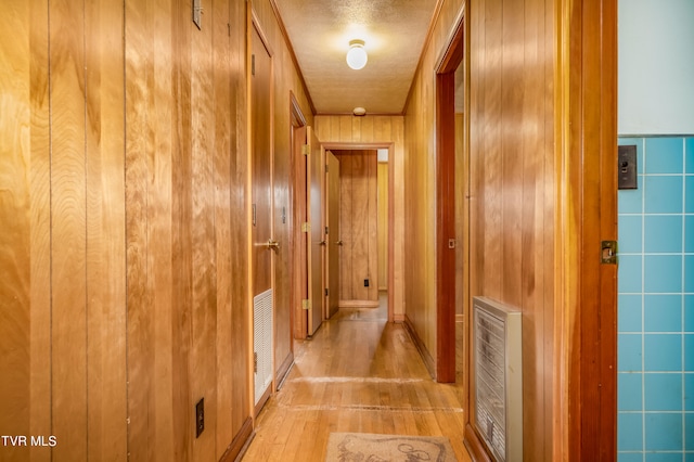 hallway with a textured ceiling, heating unit, wood walls, and light hardwood / wood-style floors