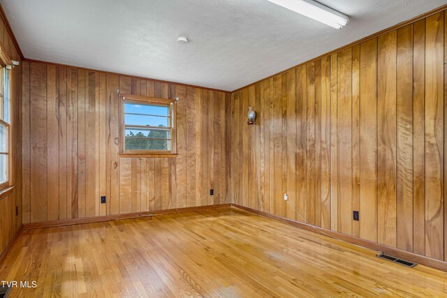 empty room with a textured ceiling, wood walls, and hardwood / wood-style floors