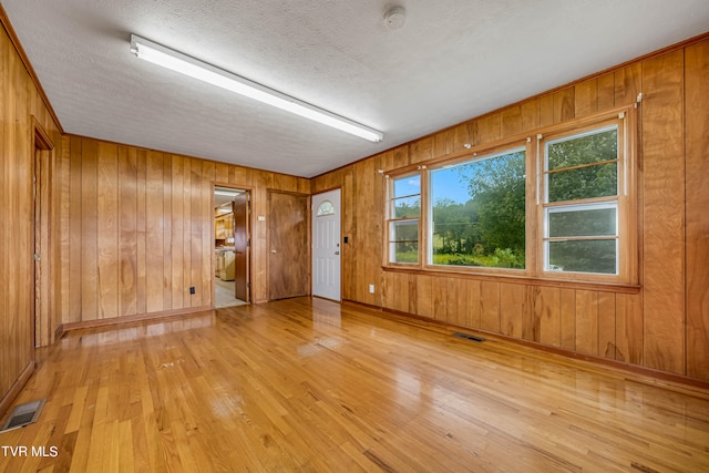 spare room with a textured ceiling, wood walls, and light hardwood / wood-style floors