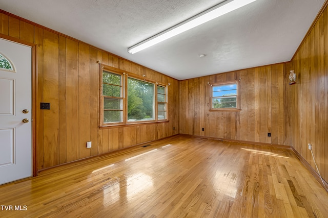 empty room featuring a textured ceiling, wood walls, and light hardwood / wood-style floors