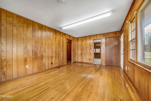 empty room featuring light wood-type flooring, wooden walls, and a textured ceiling