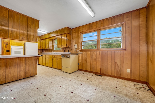 kitchen featuring wooden walls, white appliances, sink, kitchen peninsula, and a textured ceiling