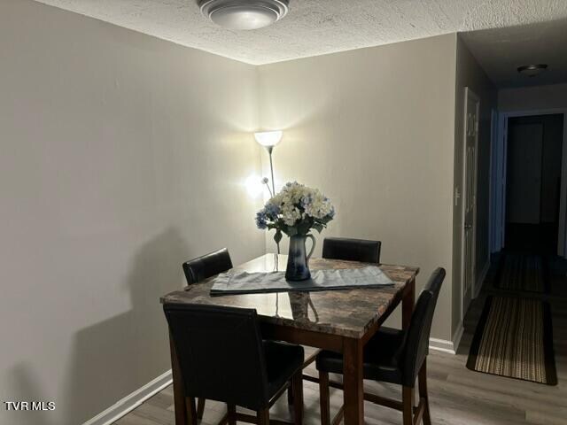 dining area with a textured ceiling, baseboards, and wood finished floors