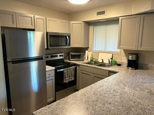 kitchen featuring stainless steel appliances, visible vents, a sink, and gray cabinetry