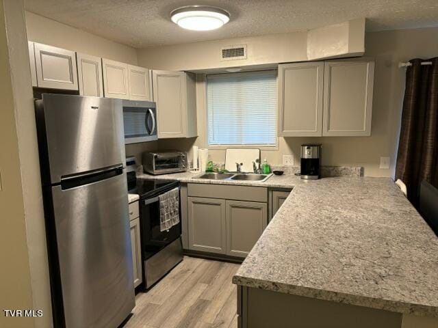 kitchen with light wood-style flooring, appliances with stainless steel finishes, a sink, a textured ceiling, and a peninsula