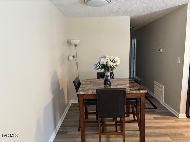 dining area featuring light wood-style floors, baseboards, visible vents, and a textured ceiling