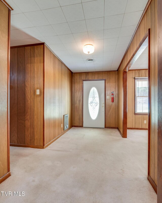 foyer entrance featuring wooden walls and light carpet