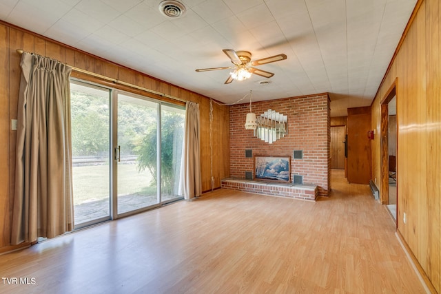 unfurnished living room featuring light hardwood / wood-style flooring, wooden walls, a fireplace, and ceiling fan