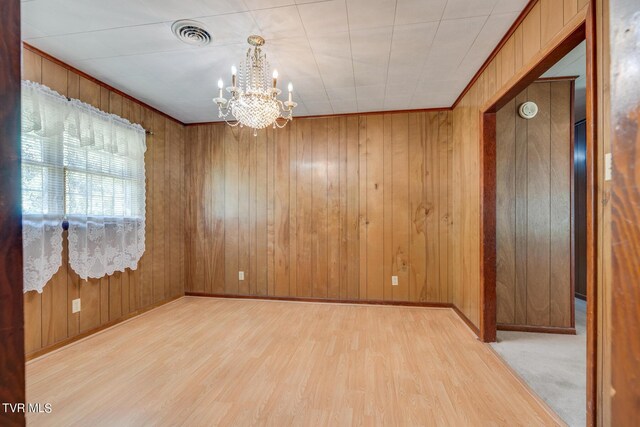 unfurnished room with light hardwood / wood-style flooring, wooden walls, and a notable chandelier