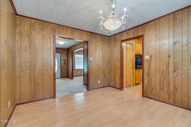 unfurnished room with an inviting chandelier, light wood-type flooring, and wood walls