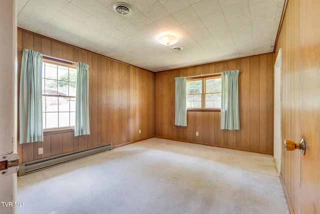 carpeted spare room featuring a baseboard radiator, wooden walls, and plenty of natural light