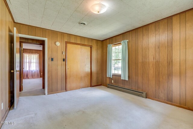 unfurnished bedroom with a closet, light carpet, a baseboard radiator, and wooden walls