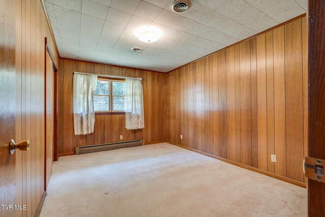 carpeted empty room featuring wood walls and a baseboard heating unit