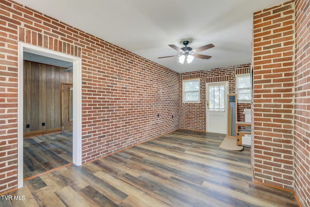 unfurnished living room with brick wall, ceiling fan, and dark wood-type flooring