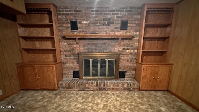 unfurnished living room with a brick fireplace, wooden walls, carpet, and a textured ceiling