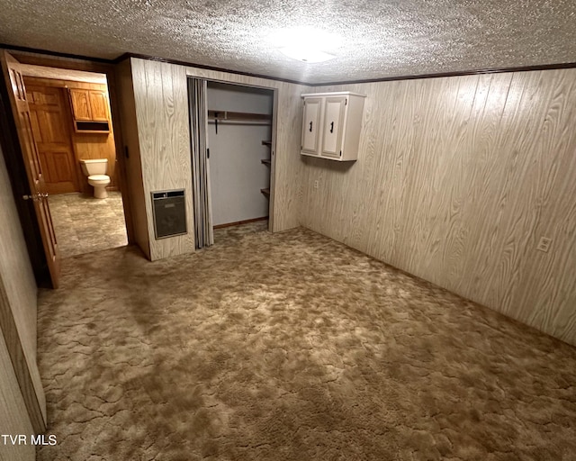 basement with heating unit, wooden walls, a textured ceiling, and carpet flooring