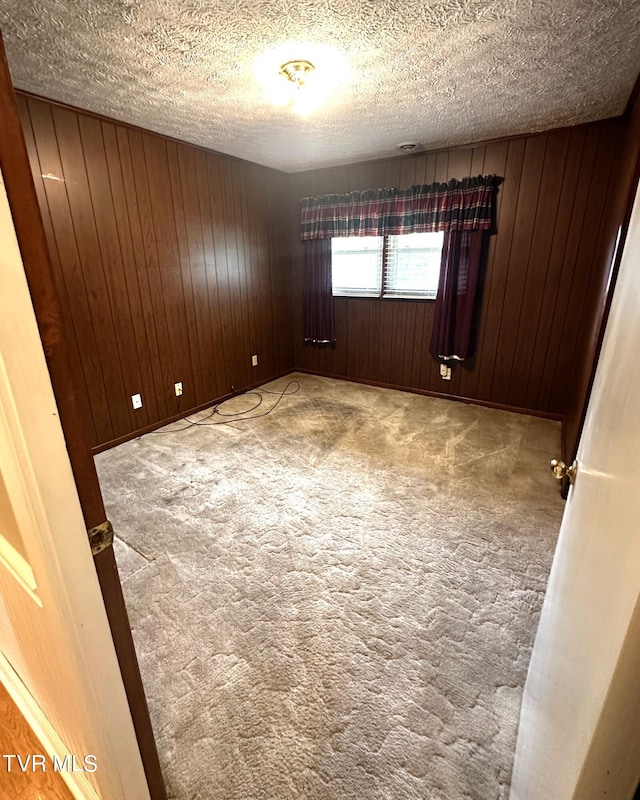 carpeted spare room featuring wood walls and a textured ceiling