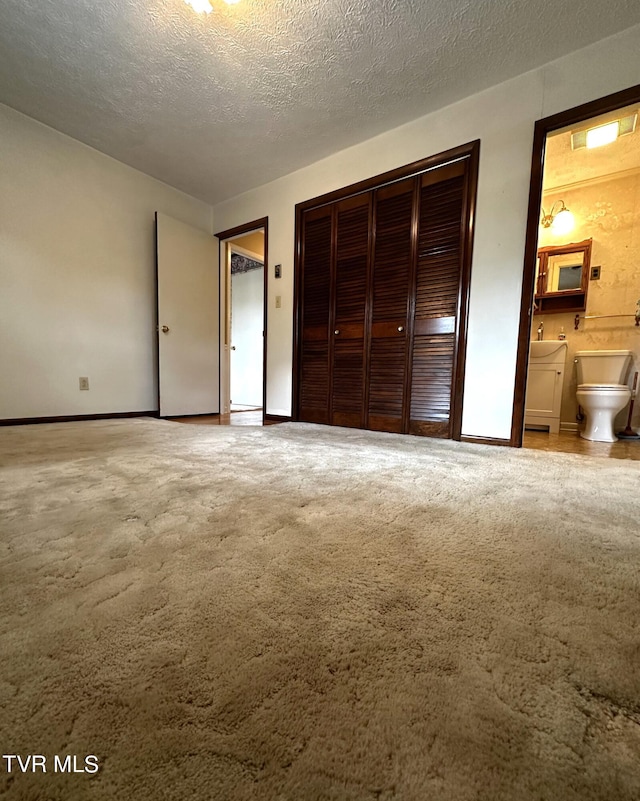 unfurnished bedroom featuring a textured ceiling, a closet, ensuite bath, and carpet flooring