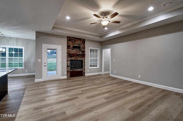 unfurnished living room featuring a fireplace, crown molding, light wood-type flooring, a raised ceiling, and ceiling fan