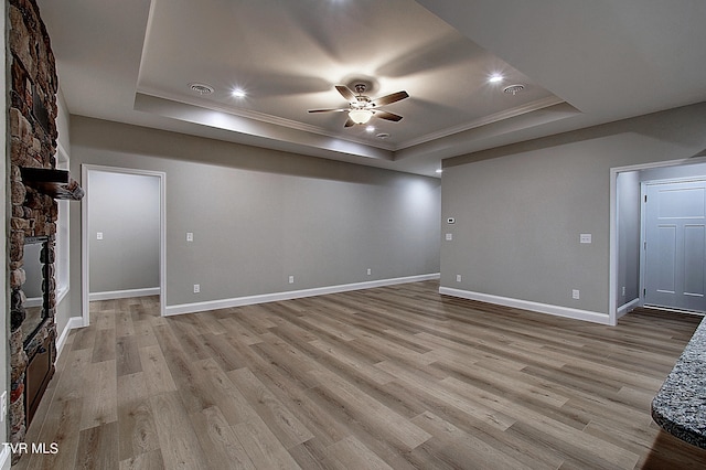 unfurnished living room featuring a raised ceiling, ceiling fan, light wood-type flooring, and a fireplace