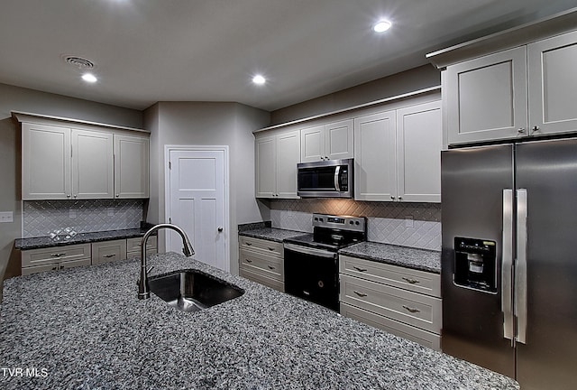 kitchen with dark stone counters, backsplash, stainless steel appliances, and sink