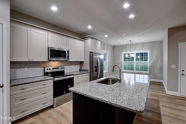 kitchen featuring appliances with stainless steel finishes, light hardwood / wood-style floors, a notable chandelier, sink, and a center island with sink