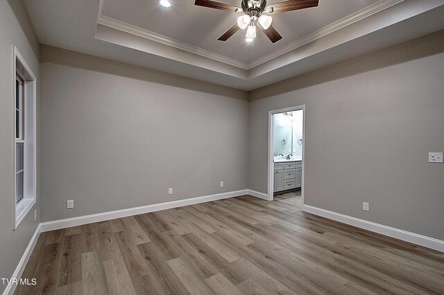 empty room featuring light wood-type flooring, crown molding, sink, ceiling fan, and a tray ceiling