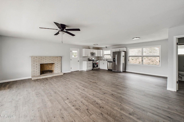 unfurnished living room with a textured ceiling, a brick fireplace, sink, ceiling fan, and dark hardwood / wood-style floors