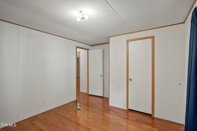 unfurnished bedroom with a textured ceiling, ornamental molding, and hardwood / wood-style flooring