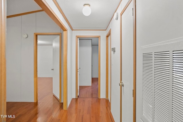 hallway featuring light wood-type flooring, ornamental molding, and a textured ceiling