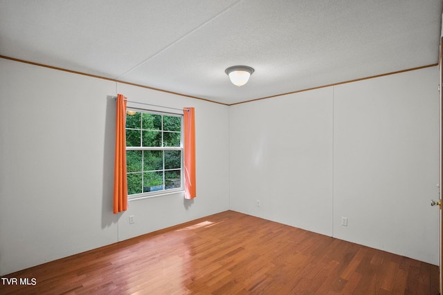 empty room featuring a textured ceiling, ornamental molding, and hardwood / wood-style flooring