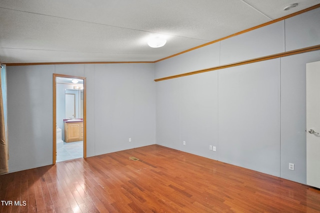 spare room featuring vaulted ceiling, a textured ceiling, crown molding, and light hardwood / wood-style flooring