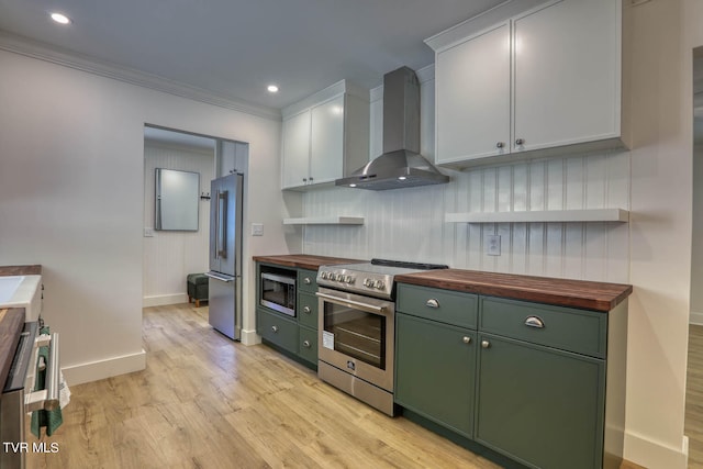 kitchen featuring wall chimney range hood, stainless steel appliances, white cabinetry, and wood counters