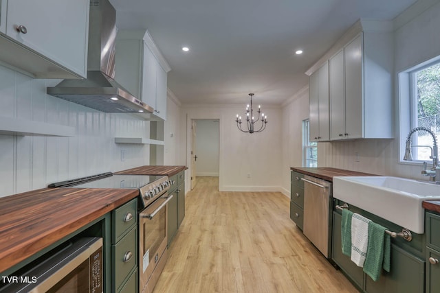 kitchen featuring white cabinetry, wood counters, hanging light fixtures, appliances with stainless steel finishes, and wall chimney range hood