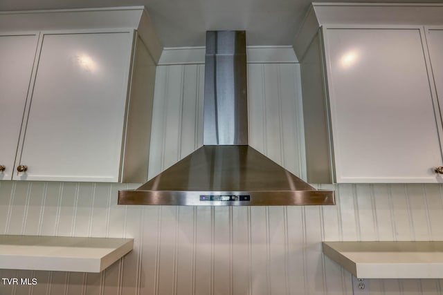 details featuring wall chimney exhaust hood and white cabinetry