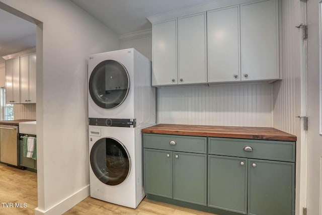 laundry area featuring crown molding, cabinets, stacked washer / dryer, and light hardwood / wood-style floors