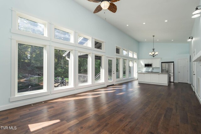 unfurnished living room featuring high vaulted ceiling, ceiling fan with notable chandelier, and dark hardwood / wood-style flooring