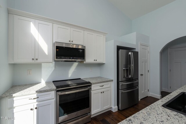 kitchen with light stone counters, appliances with stainless steel finishes, dark wood-type flooring, and white cabinetry