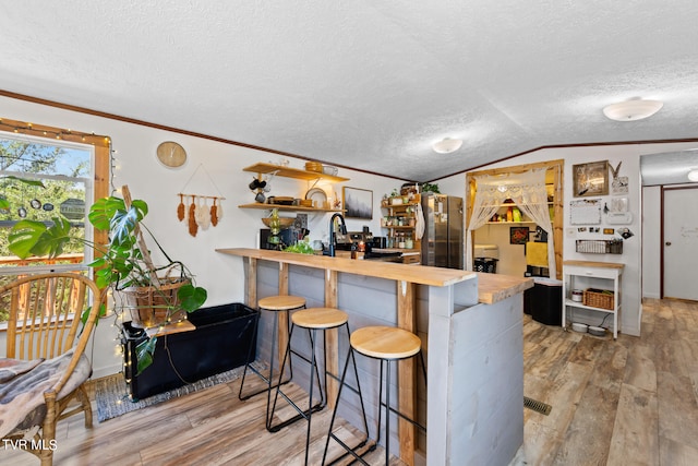 kitchen with a breakfast bar, kitchen peninsula, light hardwood / wood-style flooring, and vaulted ceiling