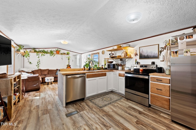 kitchen featuring appliances with stainless steel finishes, a textured ceiling, vaulted ceiling, light hardwood / wood-style floors, and white cabinetry